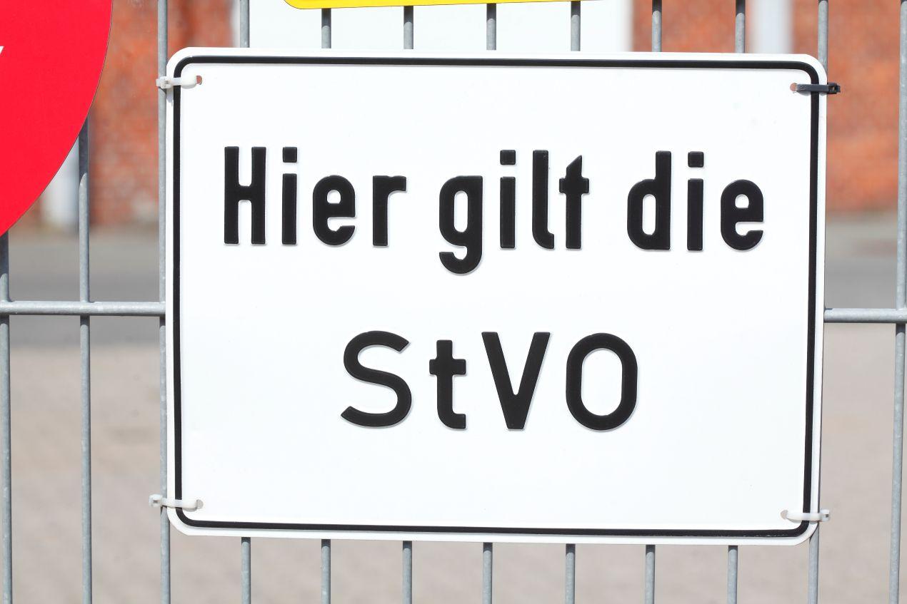Schild mit Aufschrift „Hier gilt die StVO“ vor einem Metallzaun als Symbol für rechtlich verbindliche Fahrbahnmarkierungen