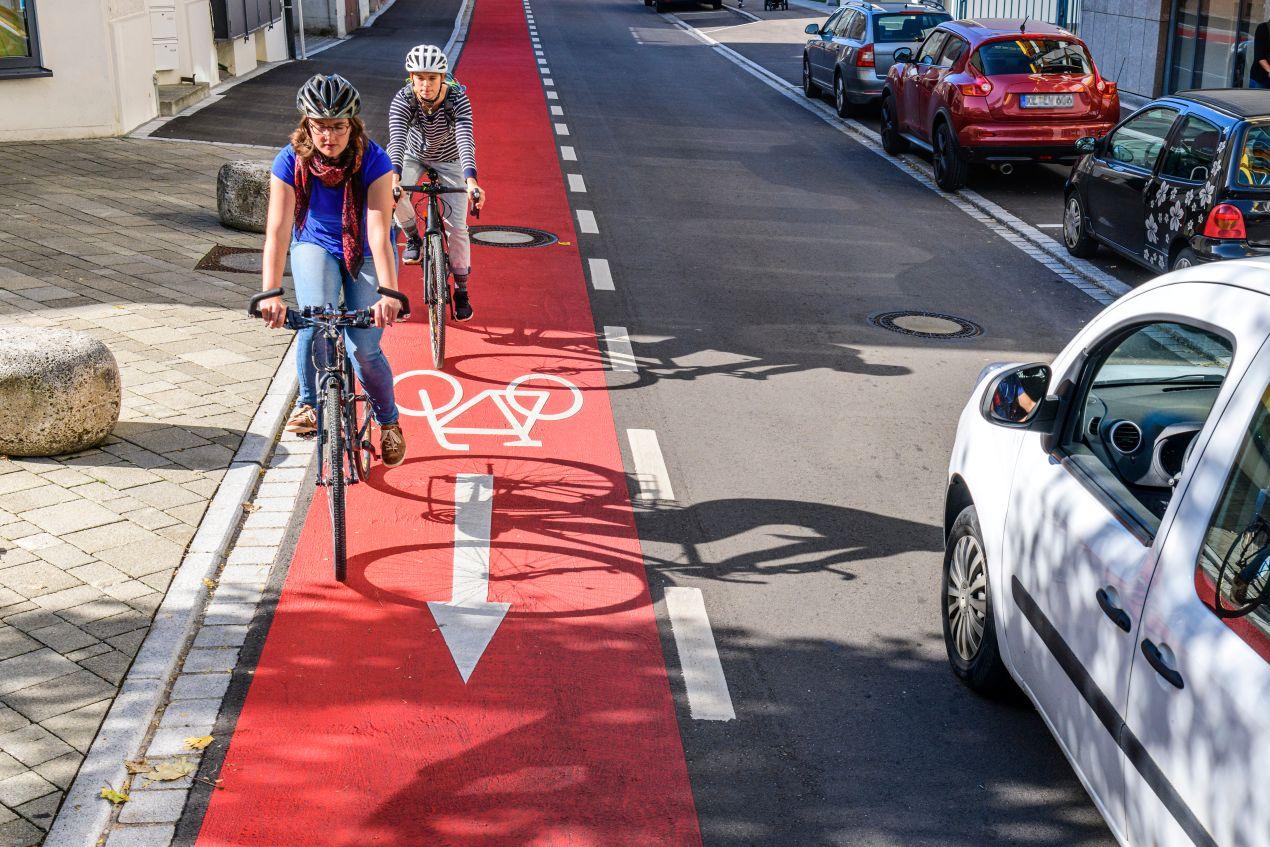 Zwei Radfahrer auf rotem Fahrradstreifen mit weissen Fahrbahnmarkierungen in einer städtischen Einbahnstraße