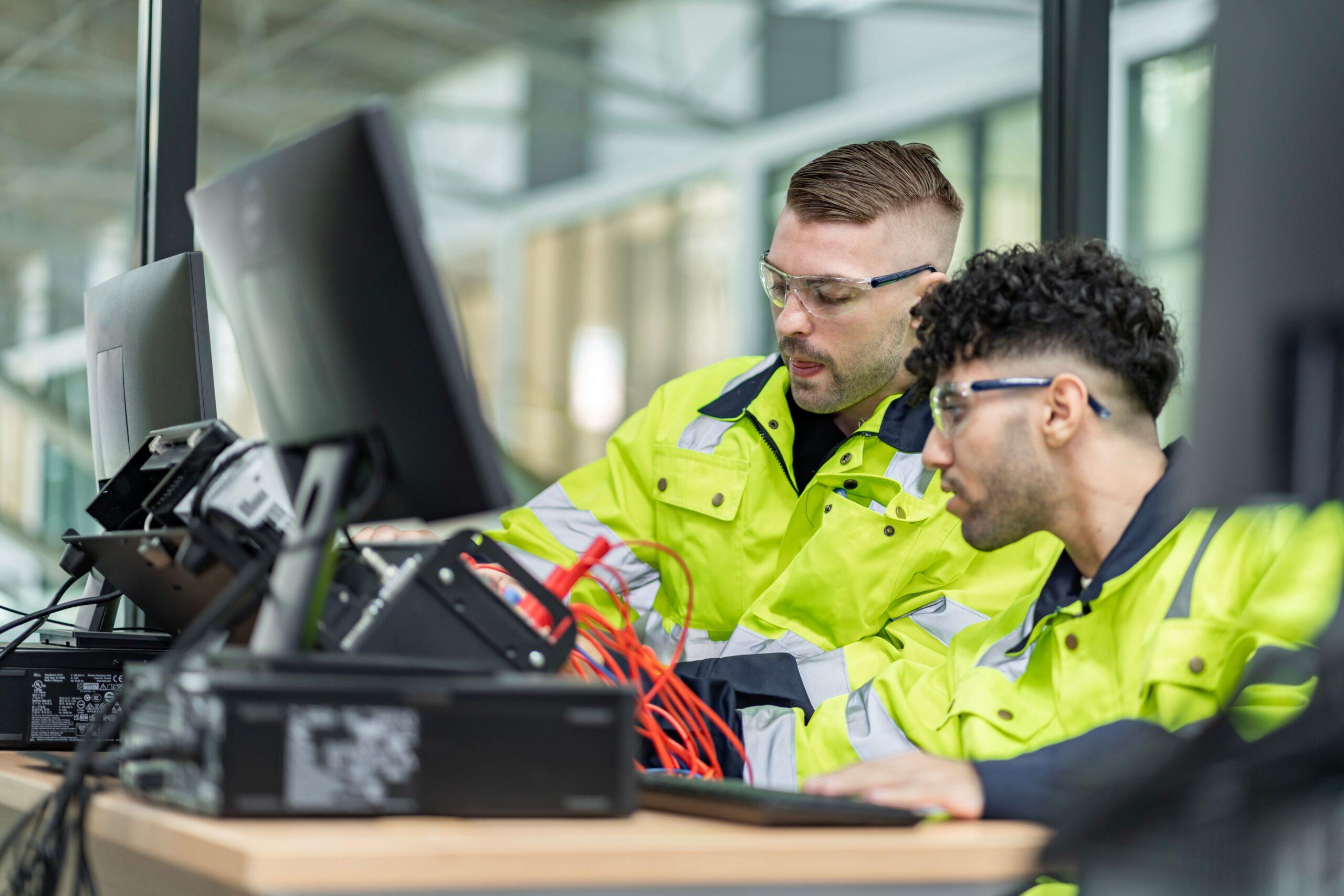 Zwei Techniker prüfen verkabelte Geräte an Monitoren – Symbol für prozesssichere industrielle Integration