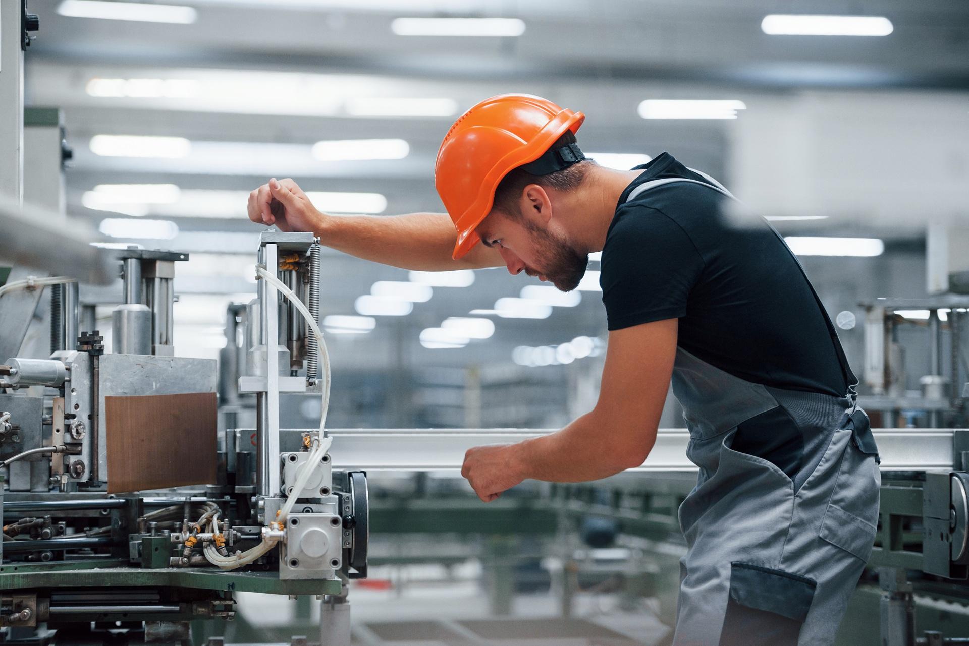 Mechaniker mit Schutzhelm prüft Maschine in Produktion | Spannrolle für Keilriemen