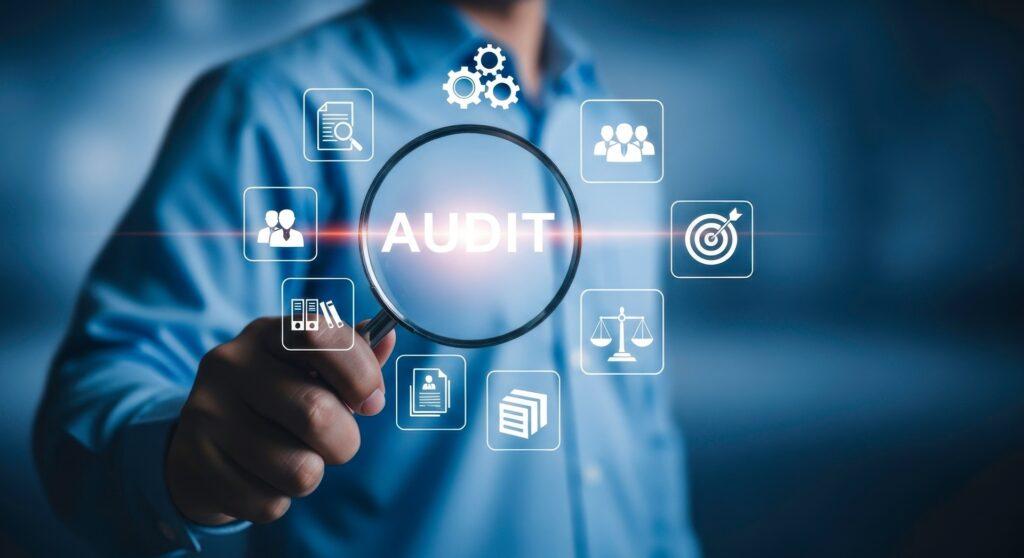 Person hält Lupe vor Audit-Symbolen | Compliance Anwalt